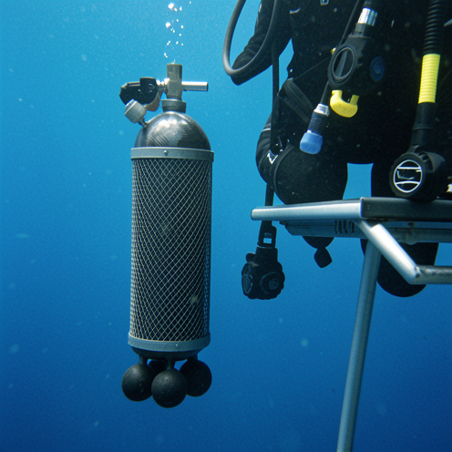 Bouteille de plongée en fibre de carbone accompagnée de poids de lestage dans un environnement sous-marin bleu.